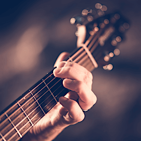child's hand playing a chord on a guitar neck